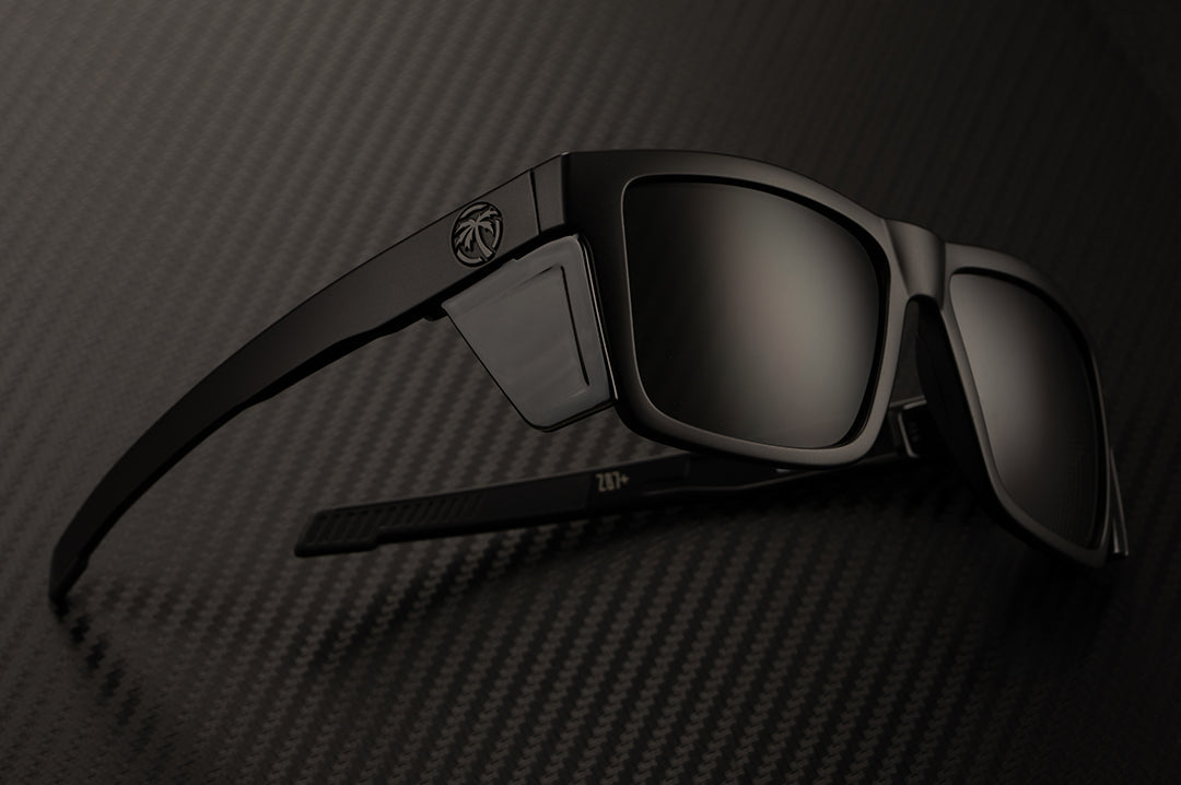 Heat Wave Visual Performance Vise Sunglasses with black frame, blacks lenses and black side shields laying on a table.