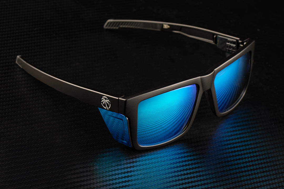 Sitting on a table is the Heat Wave Visual Performance Vise Sunglasses with black frame, galaxy blue lenses and matching colored side shields.